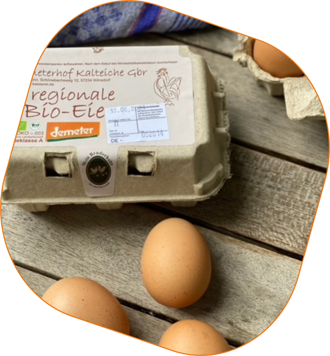 KI generiert: Das Bild zeigt eine Eierverpackung mit der Aufschrift "Regionale Bio-Eier" sowie einige lose braune Eier auf einem Holztisch. Im Hintergrund ist ein Teil eines blauen Stoffes zu sehen.