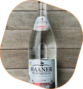 KI generiert: Das Bild zeigt eine Flasche Haaner Felsenquelle Mineralwasser auf einer Holzoberfläche. Die Flasche enthält kohlensäurehaltiges Wasser und ist klar etikettiert.