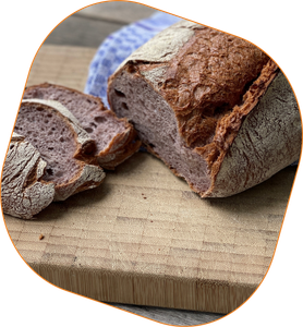 KI generiert: Das Bild zeigt ein aufgeschnittenes Brot auf einem Holzbrett, begleitet von einem blauen Tuch im Hintergrund. Der Schwerpunkt liegt auf der knusprigen Kruste und der Textur des Brotes.