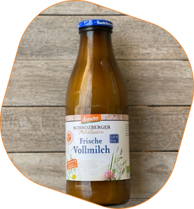 KI generiert: Das Bild zeigt eine Glasflasche mit dem Etikett "Schrozberger Milchbauern Frische Vollmilch, 3,8% Fett". Die Flasche steht vor einem Holzhintergrund.