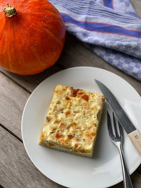KI generiert: Das Bild zeigt ein frisch gebackenes Brotlaib auf einem Holzbrett, neben einem Brotmesser. Im Hintergrund ist ein blau-weiß kariertes Tuch zu sehen.