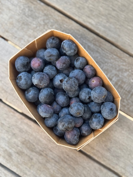 KI generiert: Ein Karton voller Blaubeeren auf einem Holztisch.